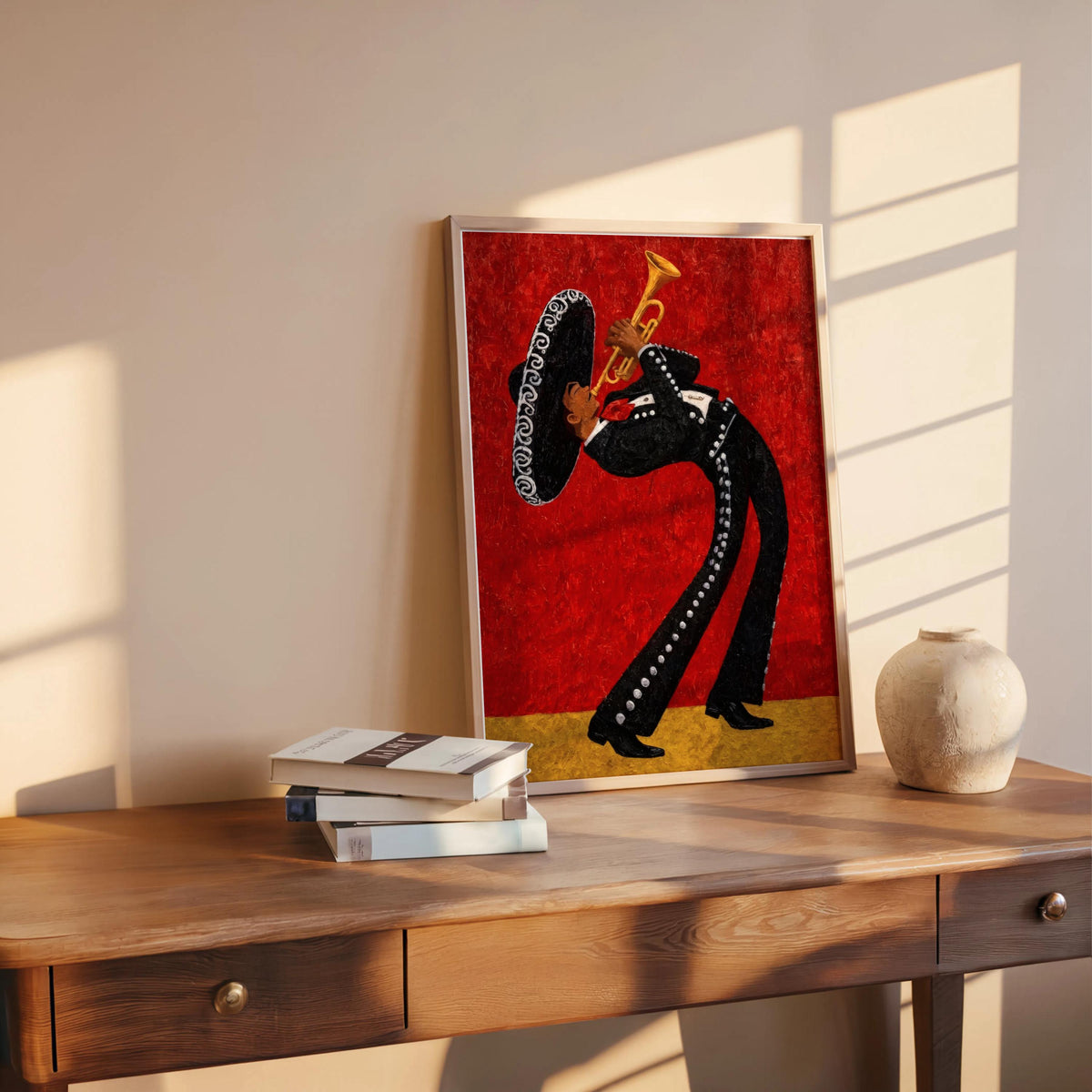 Red mariachi wall art print leaning on wood console, stacked books and a ceramic vase beside it, modern Mexican wall art vibe