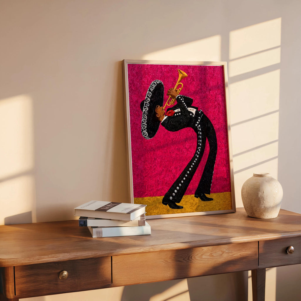 Bright magenta mariachi wall art print leaning on wooden table, vase and stacked books beside it, warm afternoon light