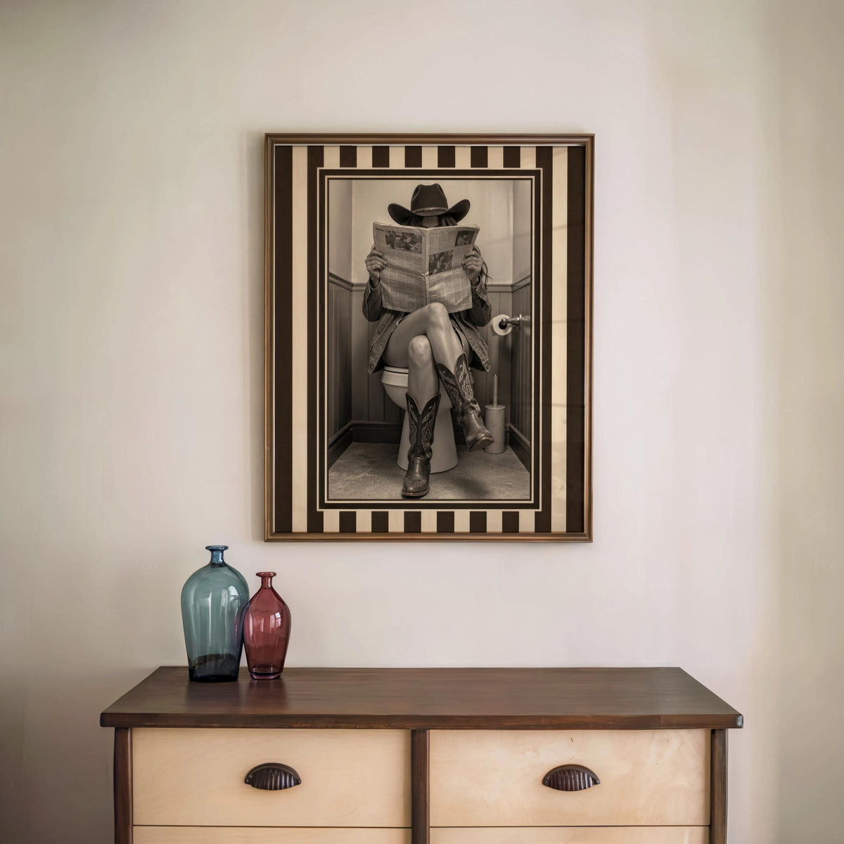 Framed vintage cowgirl toilet print above a two-drawer dresser, sepia tones and bold striped western border, funny cowgirl bathroom wall art