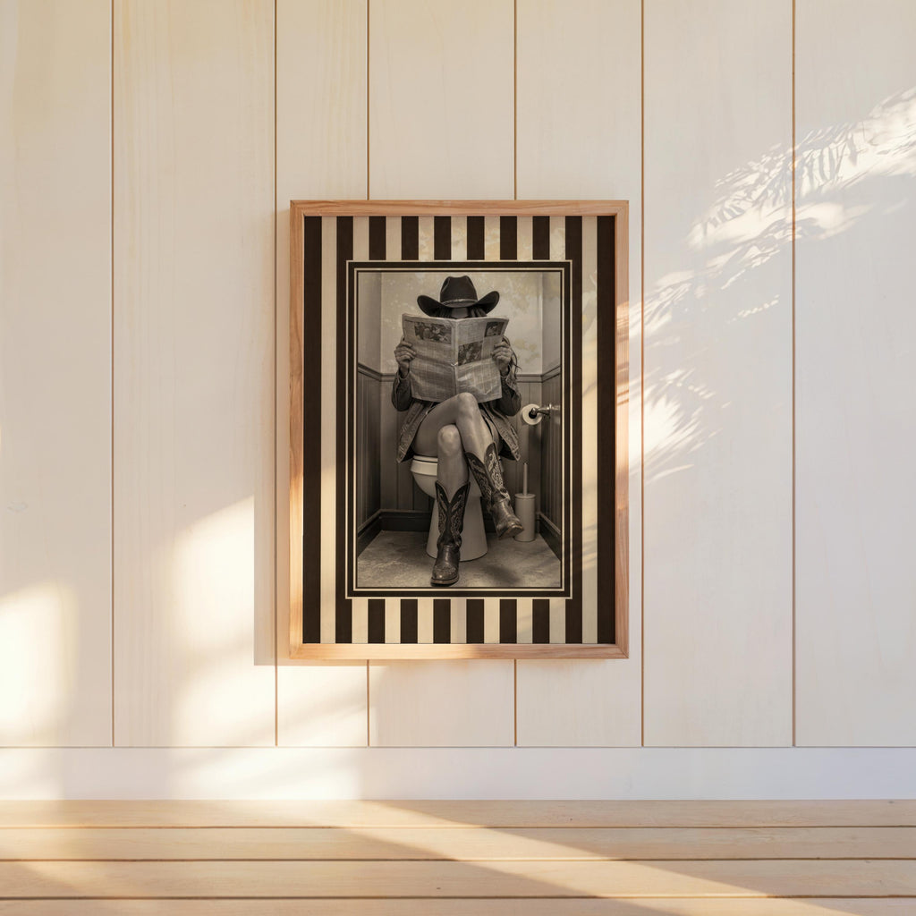 Bright paneled wall with hung vintage cowgirl print, bold striped western border and warm sunbeams, rustic western wall art, funny cowgirl bathroom wall art