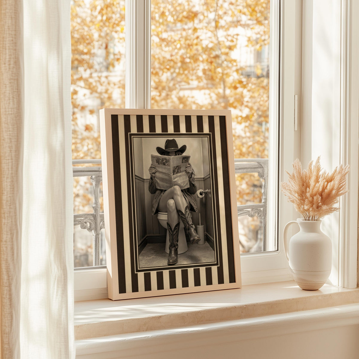 Window ledge display with framed cowgirl toilet art, autumn light and dried stems, humorous bathroom print, funny cowgirl bathroom wall art
