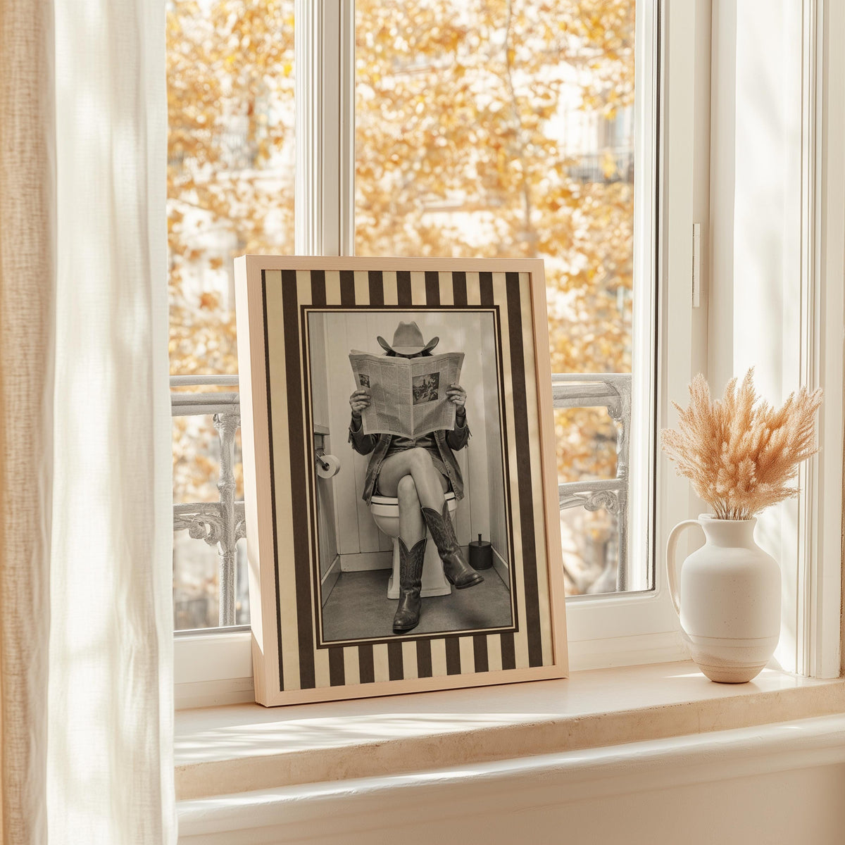 Framed sepia cowgirl print on a bright window ledge with dried blooms, funny cowgirl bathroom art, quirky restroom print