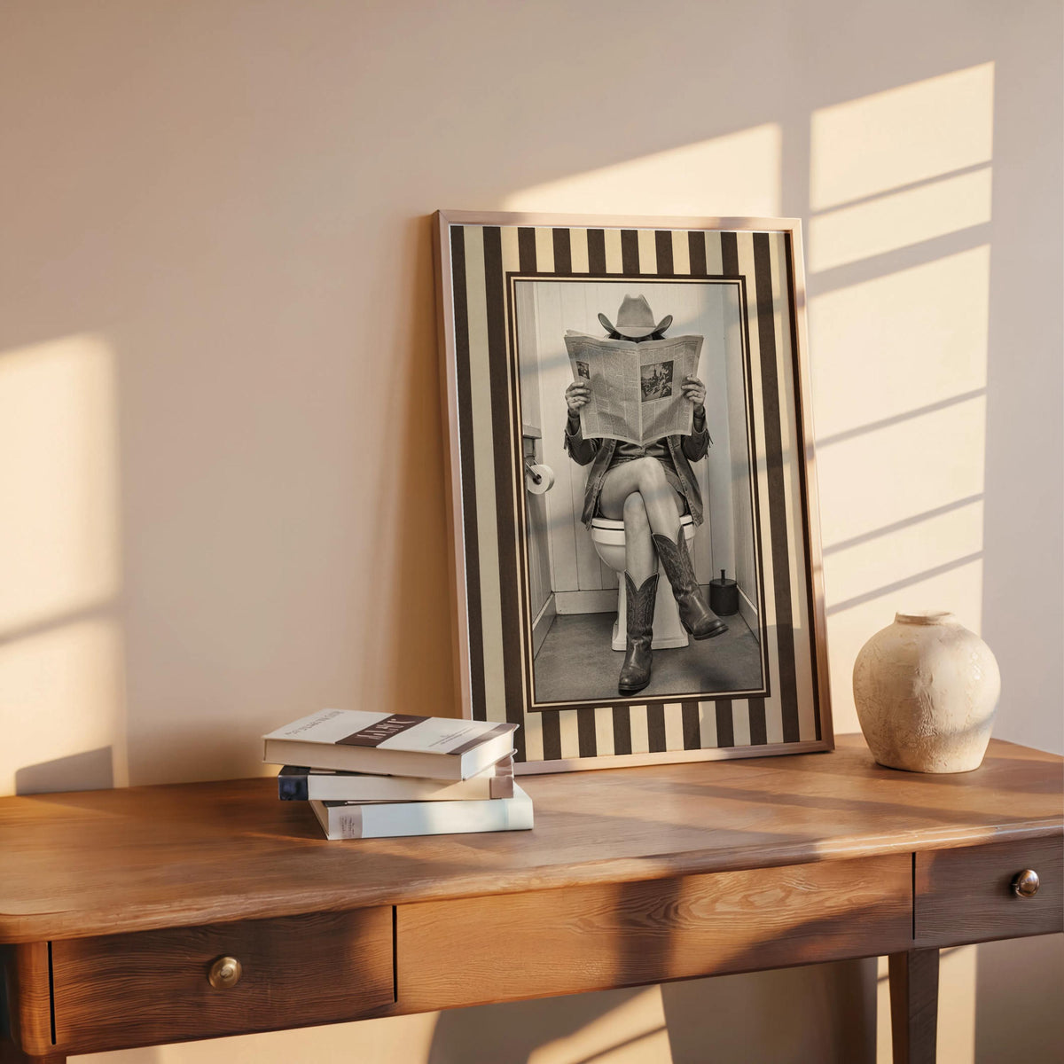 Framed warm sepia cowgirl print on a rustic bench with vase and books, funny cowgirl bathroom art, farmhouse decor