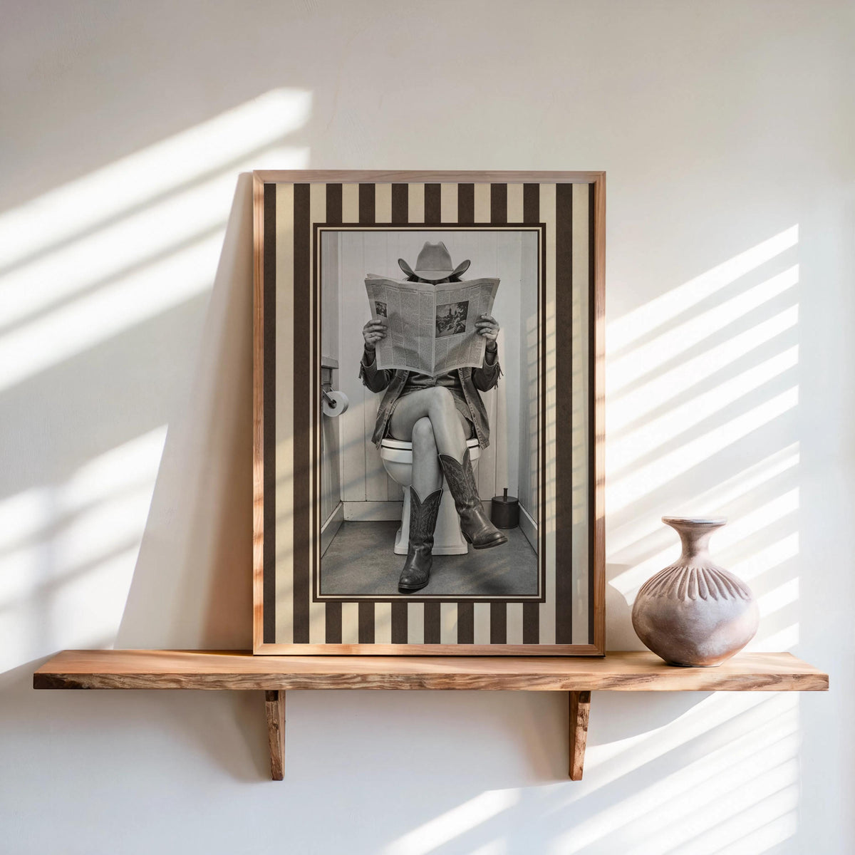 Leaning framed sepia print on a floating wood shelf, funny cowgirl bathroom art, striped border, rustic feel