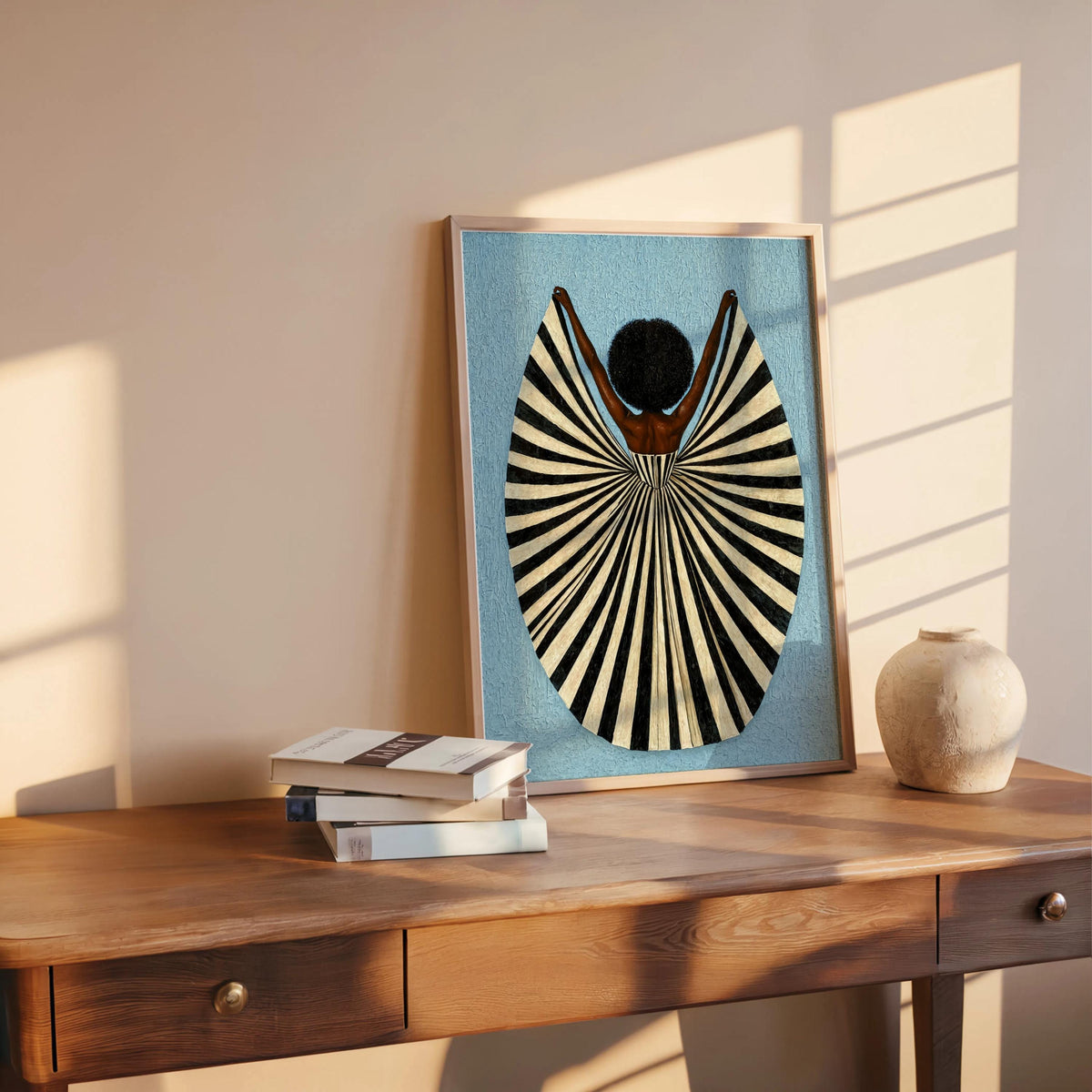 Light blue framed art on shelf, sunlit wall and stacked books, abstract female figure print, abstract black woman wall art