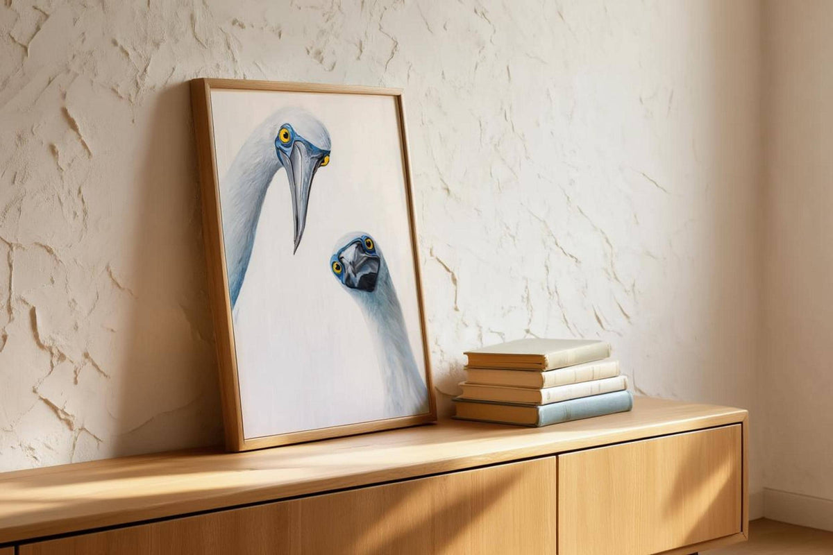 Leaning frame on textured plaster shelf with stacked books, coastal bird wall decor vibe, blue footed booby wall art print