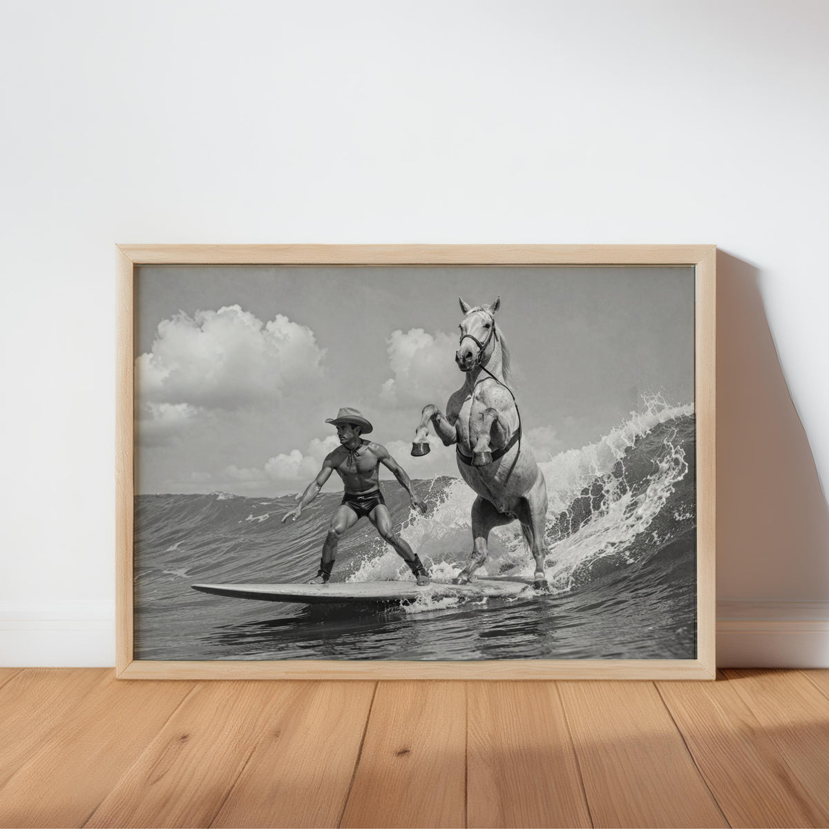 Framed black and white cowboy surfing wall art leaning on hardwood floor, light wood frame