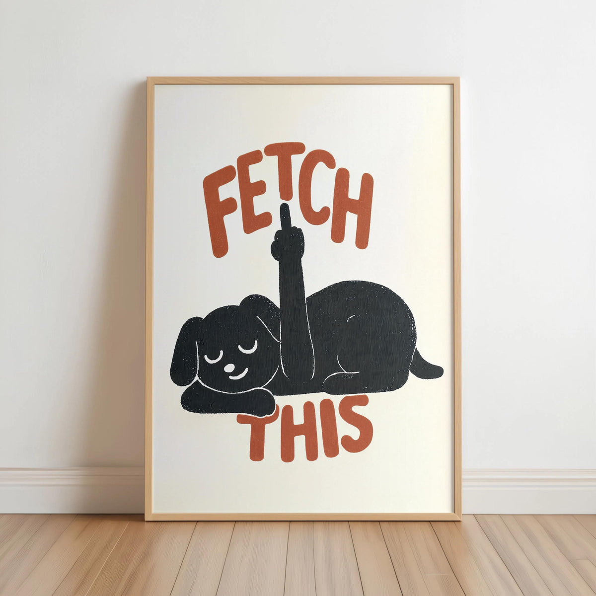 Framed cream poster propped on floor, charcoal dog silhouette and rust-orange FETCH THIS type, cheeky dog print, funny dog wall art