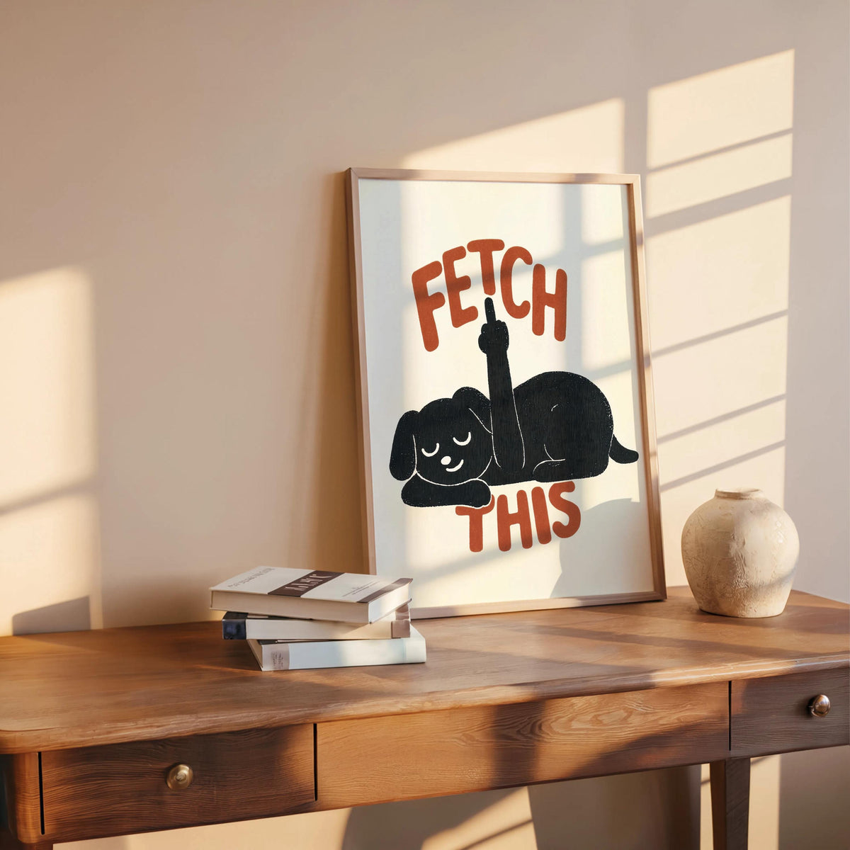 Framed poster casually leaning on a desk with warm sunlight, charcoal dog silhouette and orange text, playful dog decor
