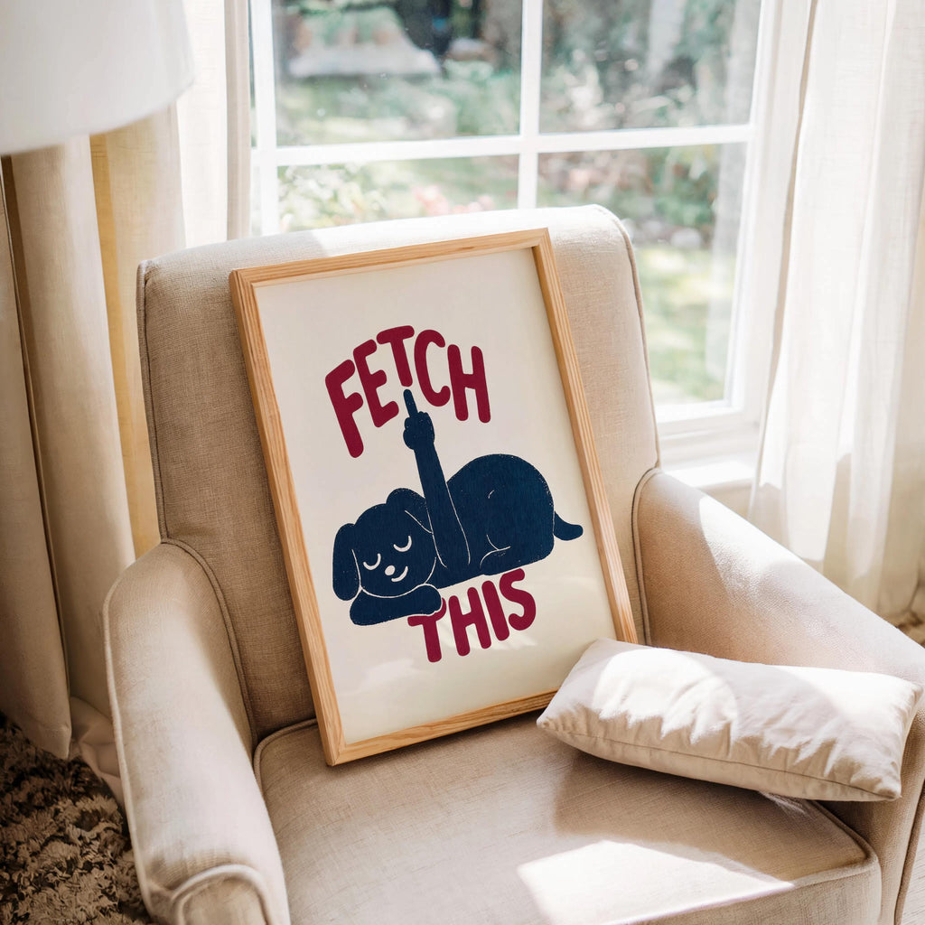 Cozy chair styling with framed print tucked into the cushion, navy dog silhouette and rust-red FETCH THIS text, funny pet wall art
