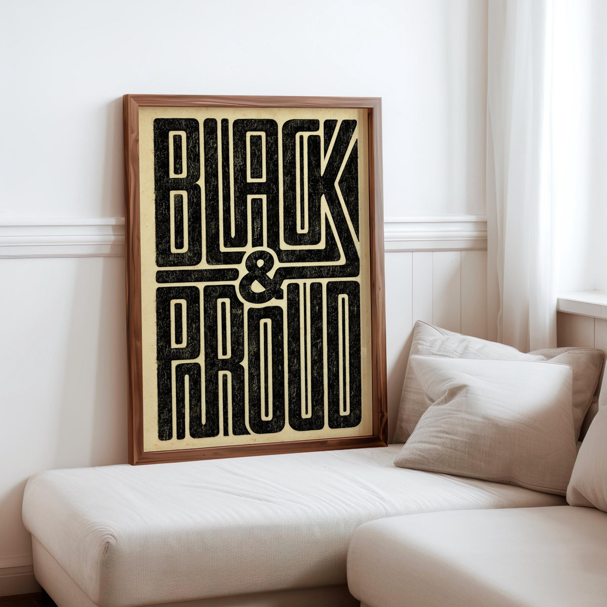Black and Proud wall art propped against cushions on a sofa, wooden frame, warm cream background, Afrocentric wall art vibe
