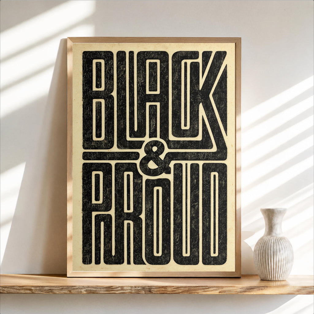 Framed Black and Proud wall art on a floating wood shelf, distressed black letters on warm cream, gold-toned paper