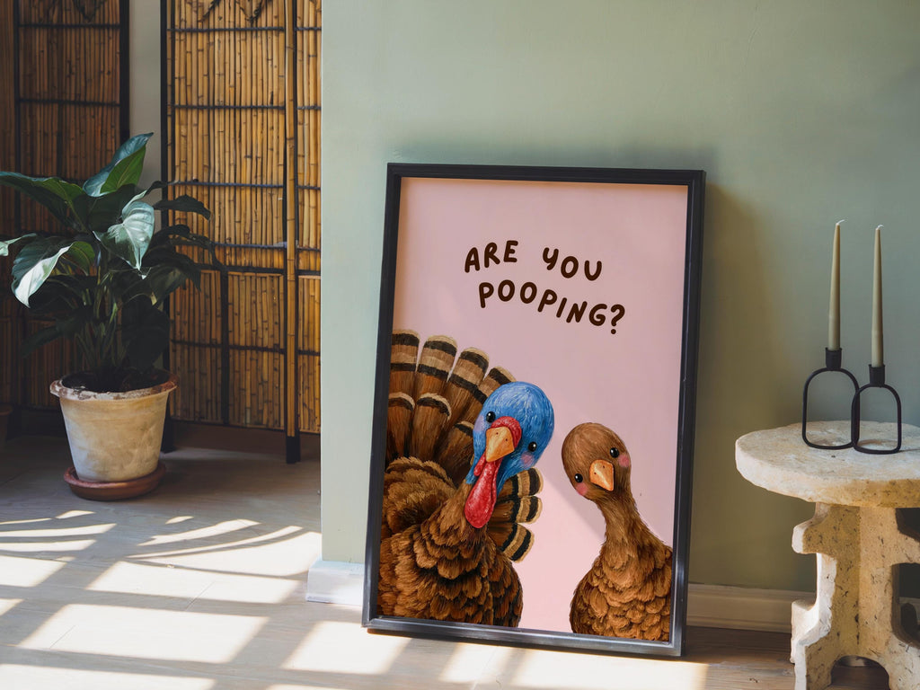 Quirky toilet sign styled as powder room wall decor, pink background funny turkey bathroom print leaning beside candles and plant