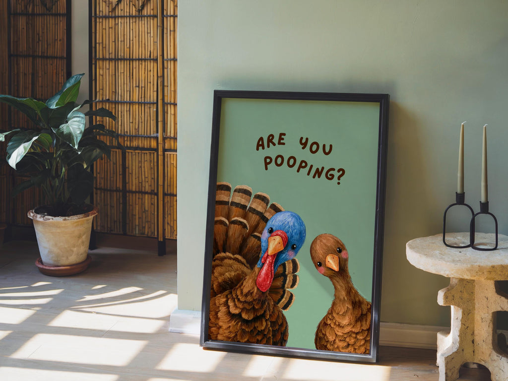Room scene with funny turkey bathroom print leaning against wall, green backdrop props, humorous restroom print styled with candles