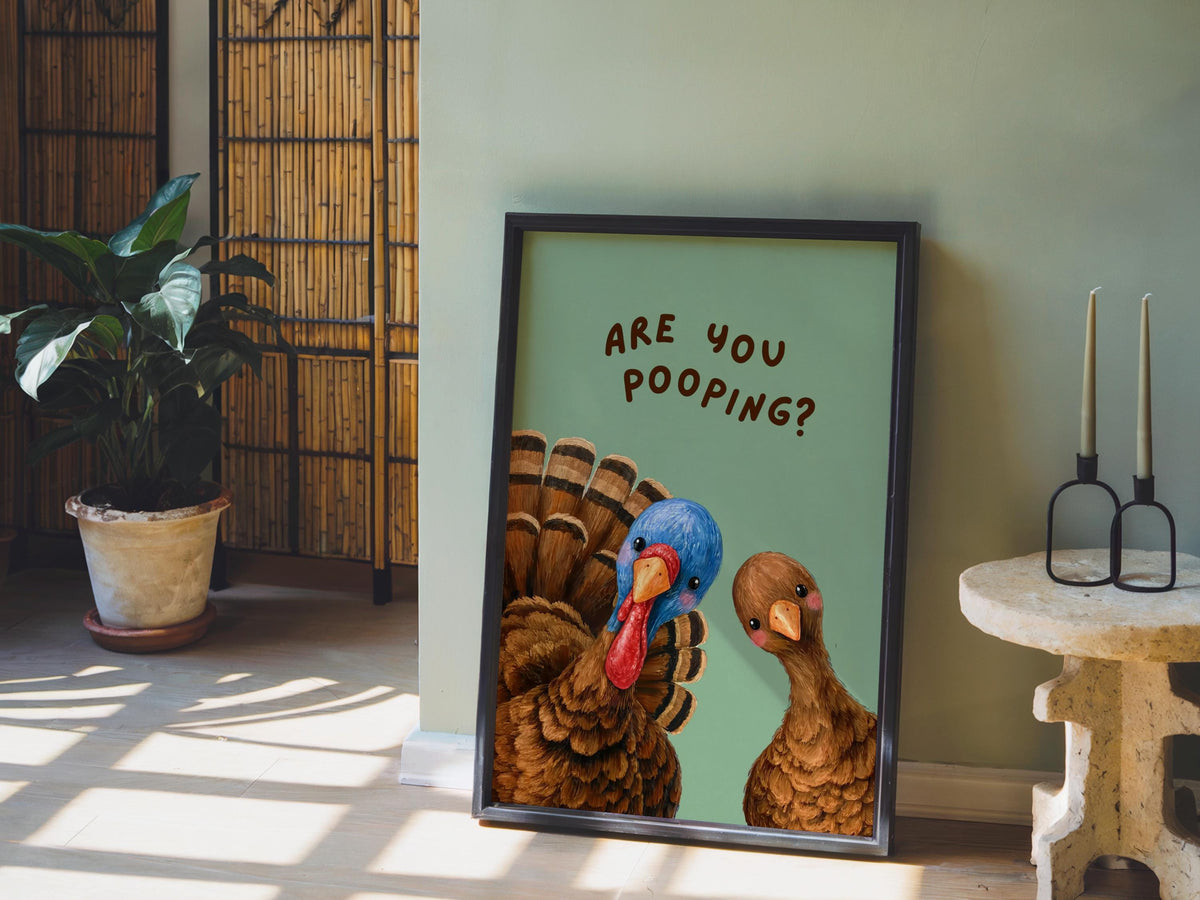 Room scene with funny turkey bathroom print leaning against wall, green backdrop props, humorous restroom print styled with candles