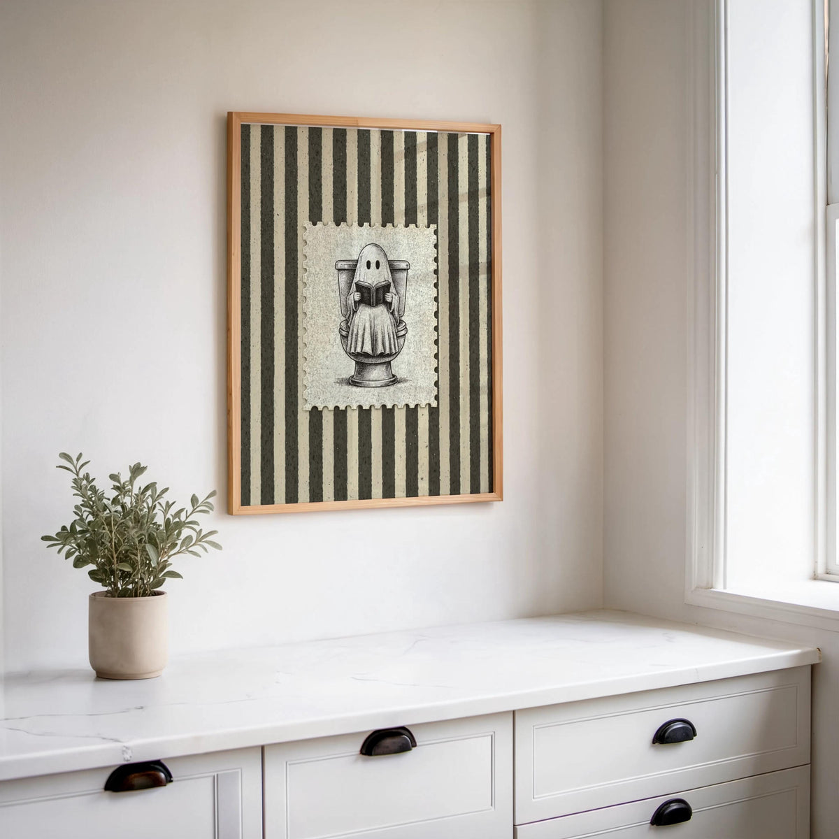 Small framed antique Halloween illustration hung above a white dresser with a potted plant, ghost bathroom art, funny bathroom wall art
