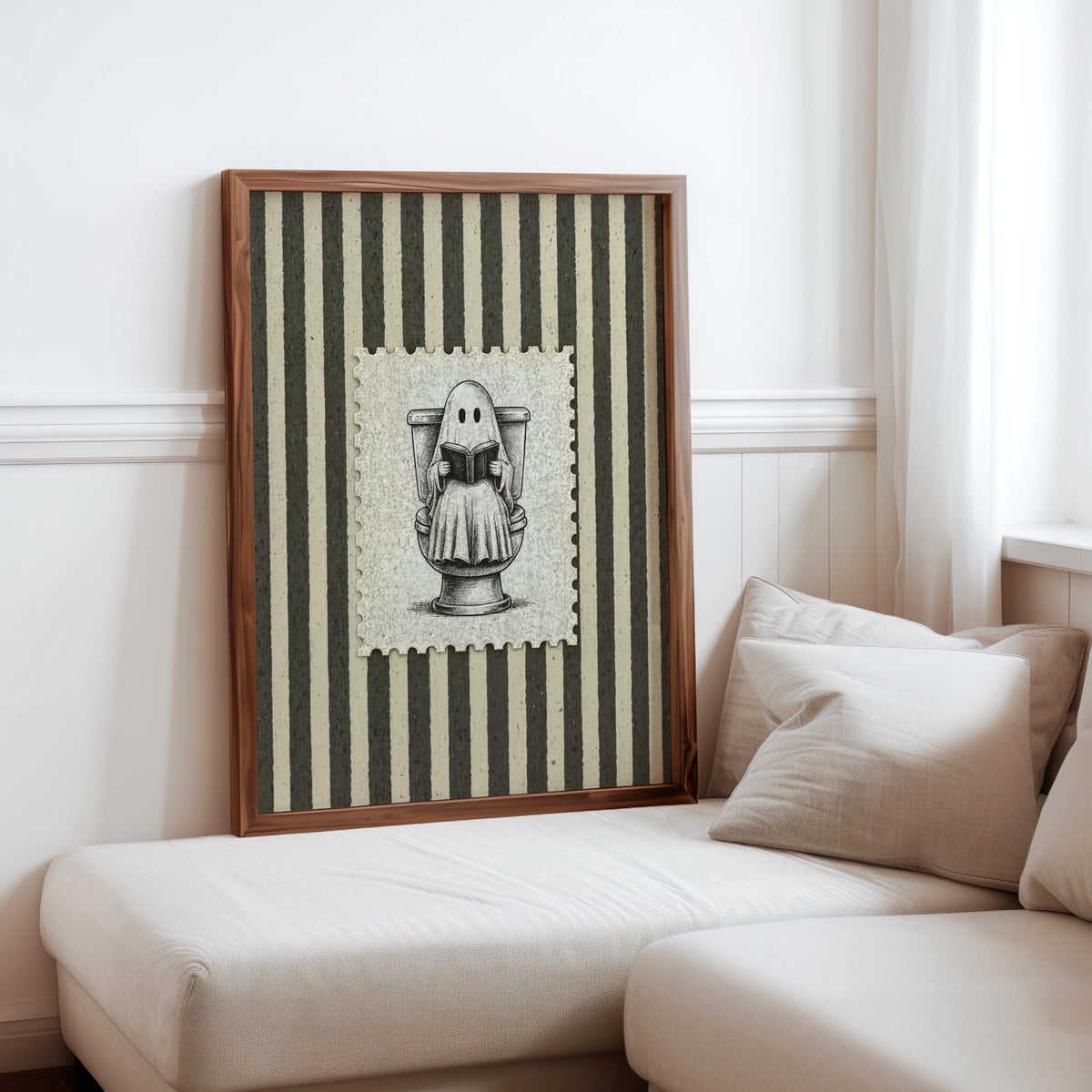 Framed ghost toilet print leaning against a cozy sofa, neutral pillows and tall stripes, quirky bathroom poster, funny bathroom wall art
