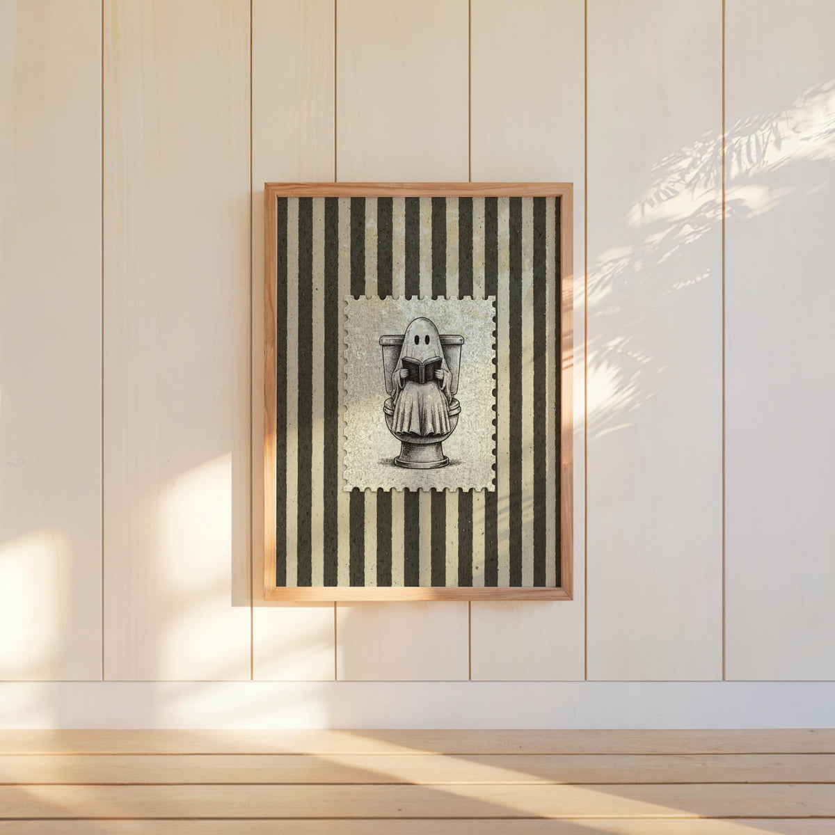 Wall-hung framed ghost reading print centered on pale paneling, charcoal stripes and vintage engraving vibe, funny bathroom wall art
