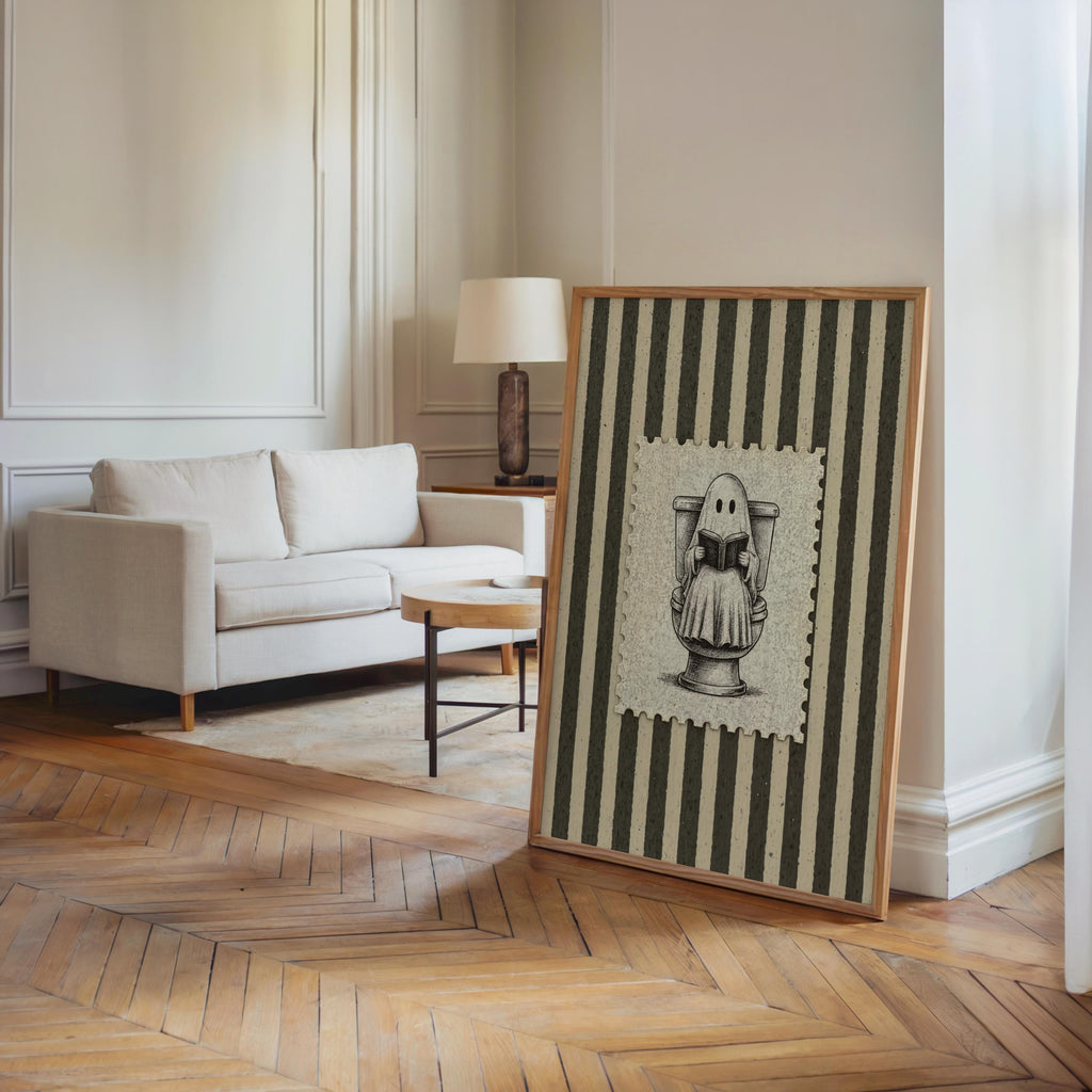 Large framed ghost reading print leaning on a bright living room floor, parquet wood and modern sofa, toilet humor wall art and funny bathroom wall art