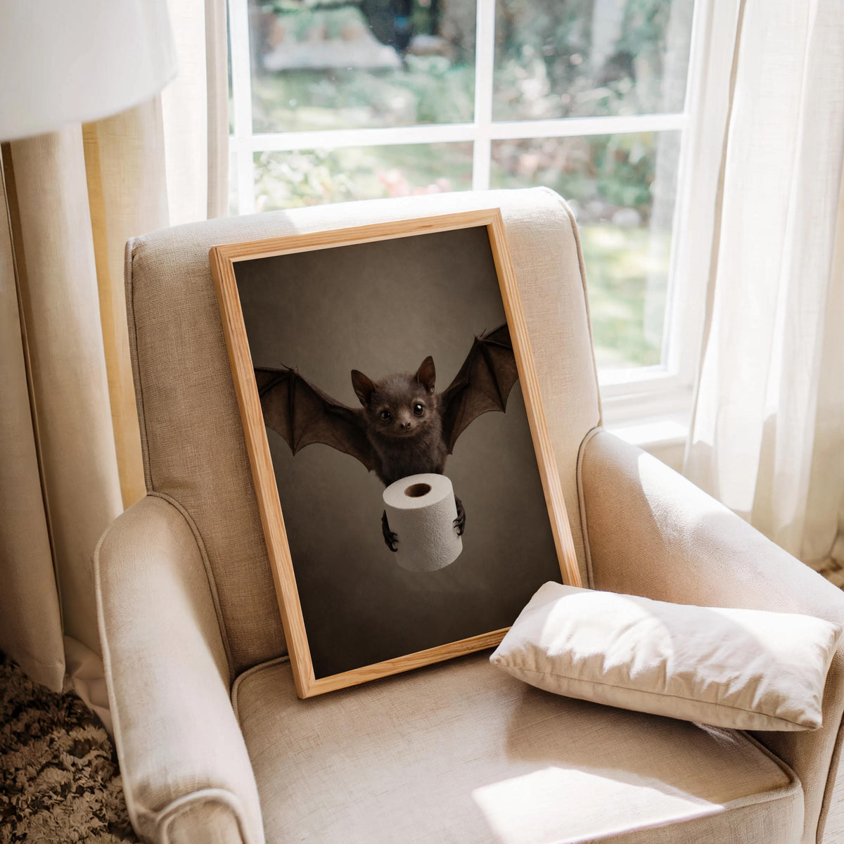 Bat print propped on a cushioned armchair by a bright window, cozy vintage staging, cute bat wall print for a powder room