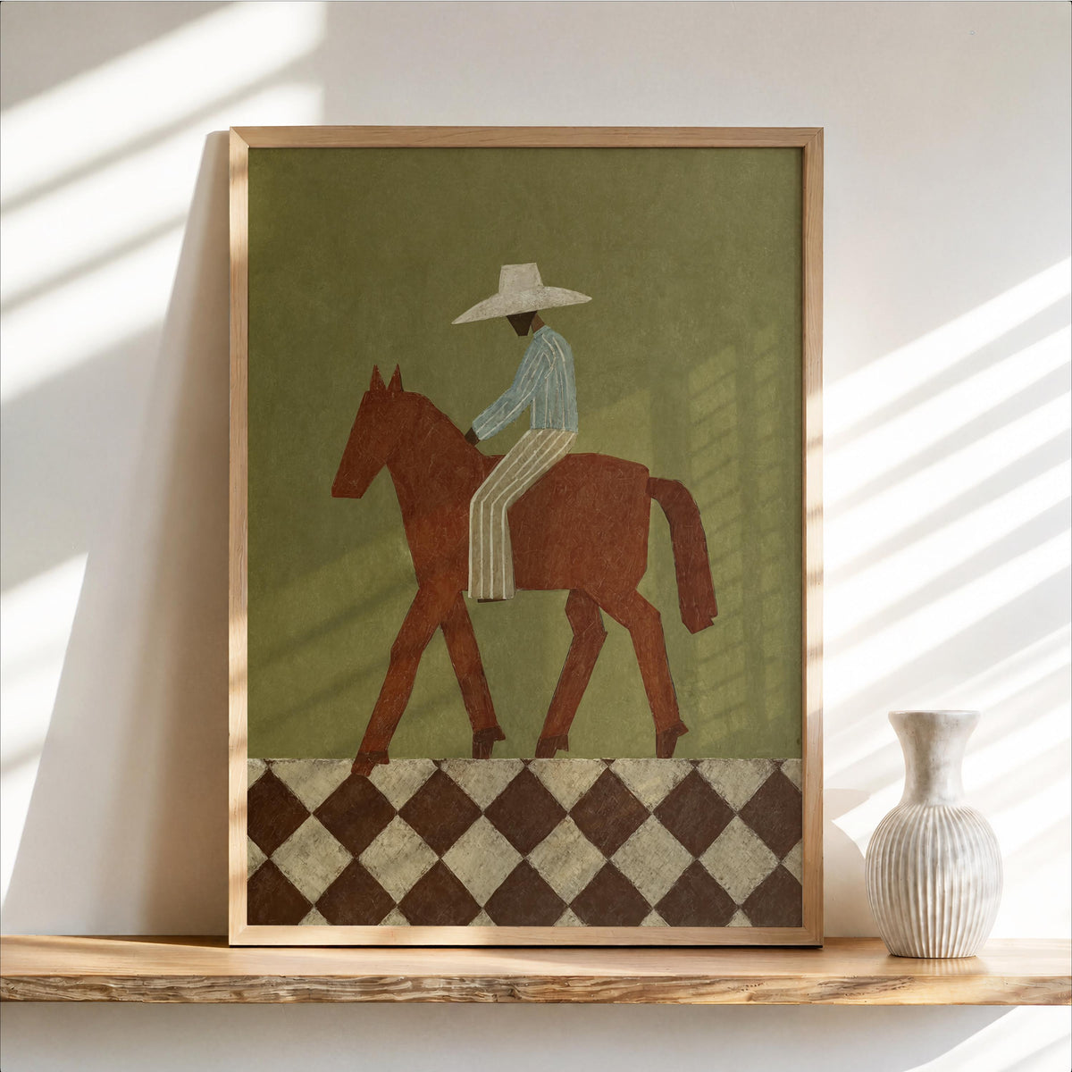 Framed abstract cowboy wall art leaning on a wooden shelf, olive background, rust horse and diamond border