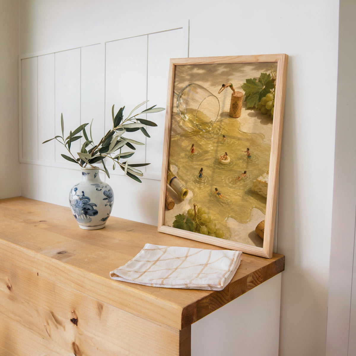 Framed print on a wooden console with vase and paper, bar cart wall art vibe, surreal wine wall art in warm tones