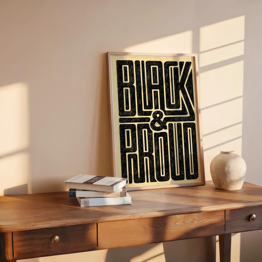 Black and Proud wall art on a midcentury desk, sunlight casting shadows, Black empowerment art with tall geometric type