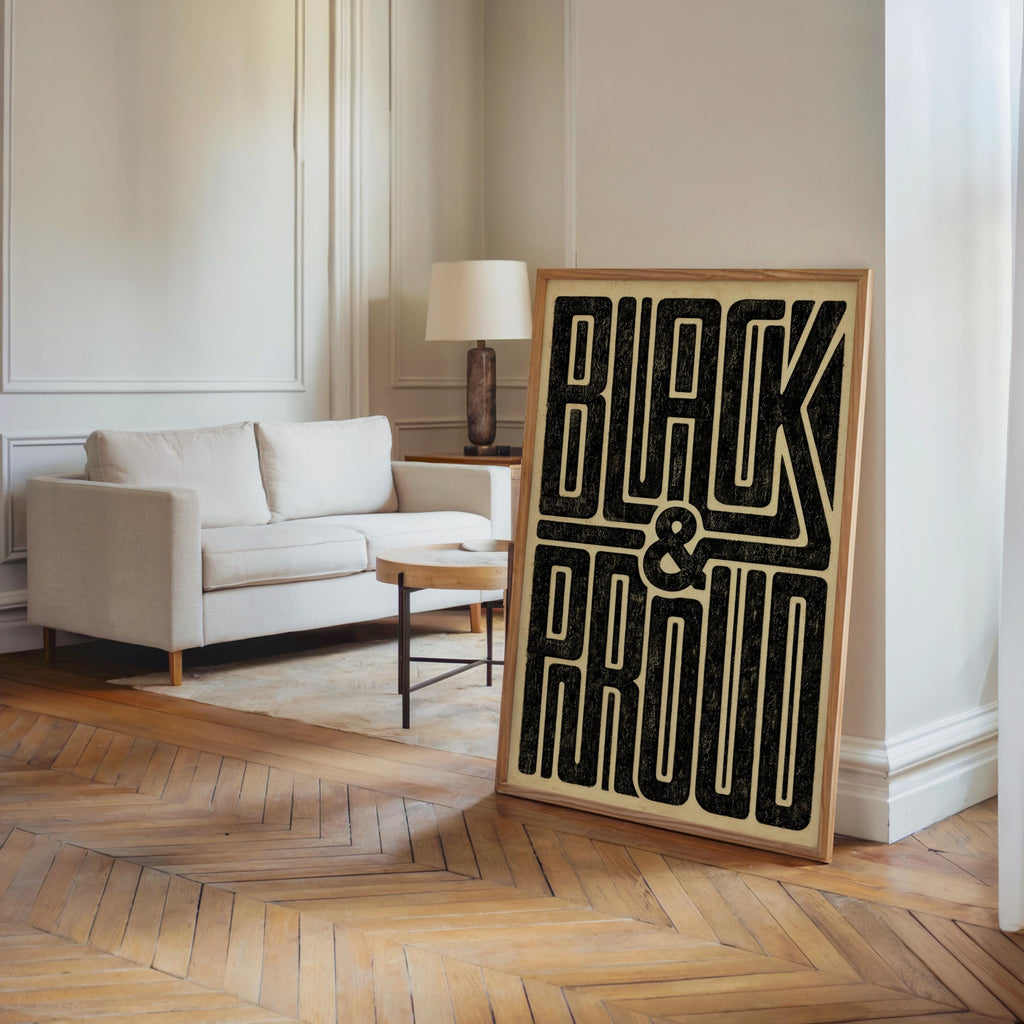 Framed Black and Proud wall art leaning near a light sofa in a bright living room, bold distressed typography on cream