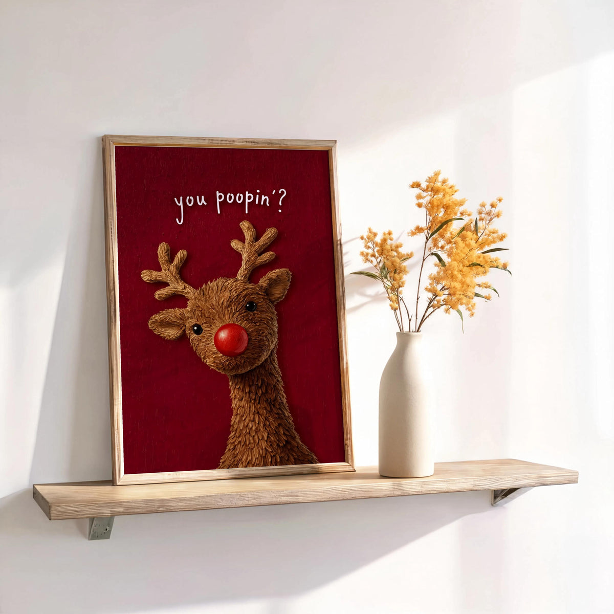 Deep red framed Rudolph leaning on a shelf, humorous Christmas bathroom wall decor, glitter nose catching the light
