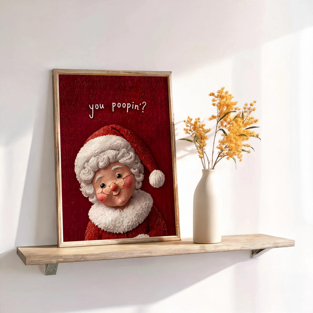 Leaning framed Mrs Claus print on shelf with dried stems, red textured background, funny Christmas bathroom wall art