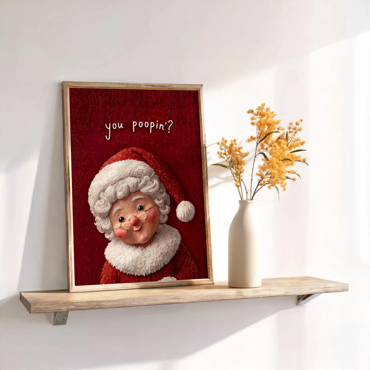 Leaning framed Mrs Claus print on shelf with dried stems, red textured background, funny Christmas bathroom wall art