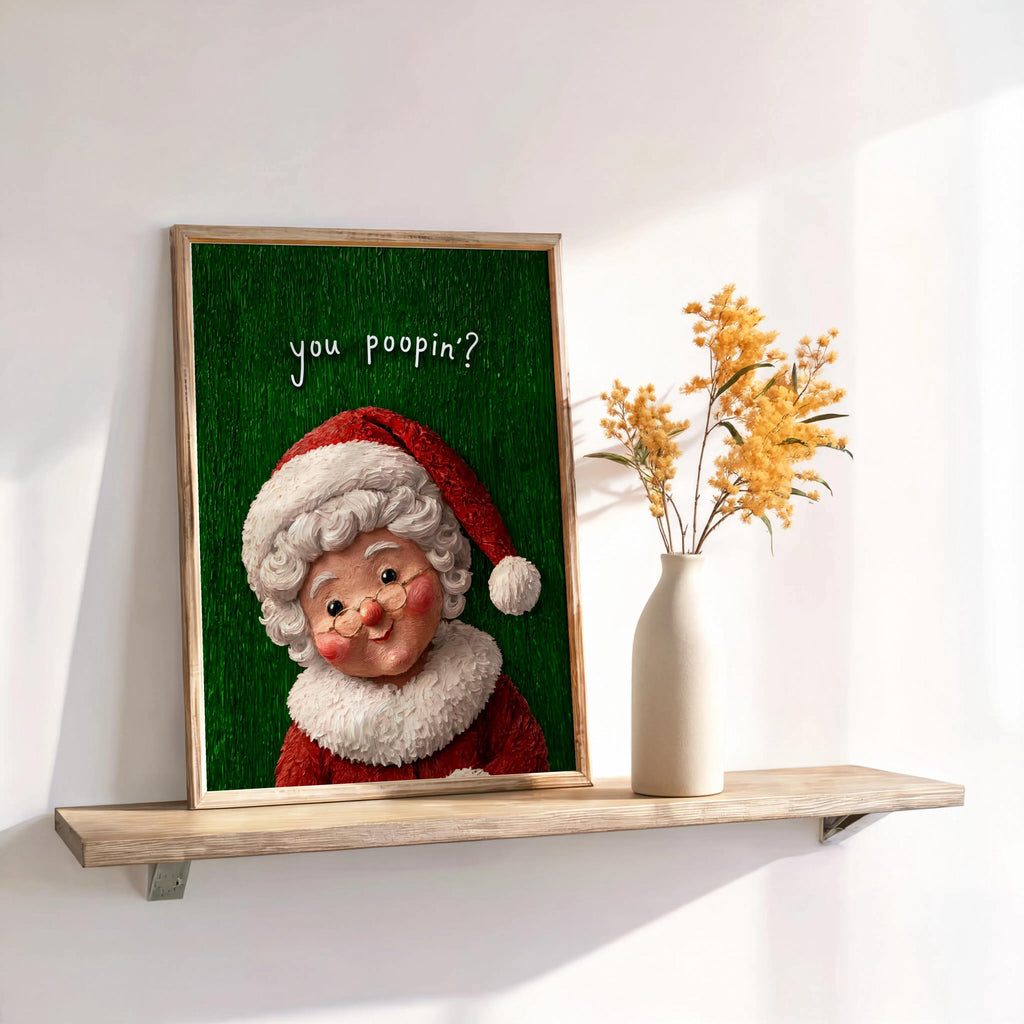 Propped green Mrs Claus print beside dried floral vase on shelf, quirky holiday bathroom art, funny Christmas bathroom wall art