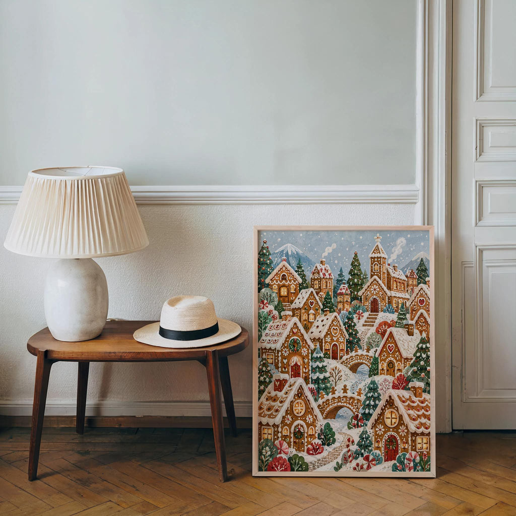 Gingerbread village wall art leaning beside a table lamp and straw hat, cozy entry vignette