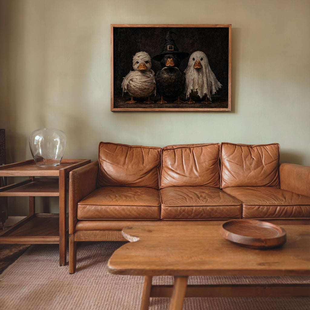Framed Halloween duck wall art hung above a leather sofa in cozy living room, vintage Halloween wall art, muted black and brown palette