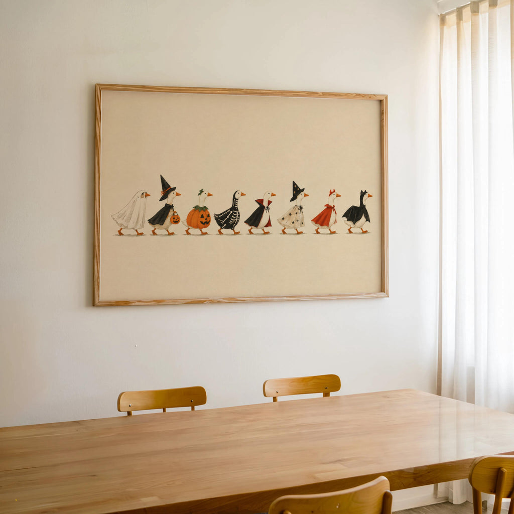 Framed Halloween duck print centered above dining table, warm cream paper, whimsical Halloween art for home