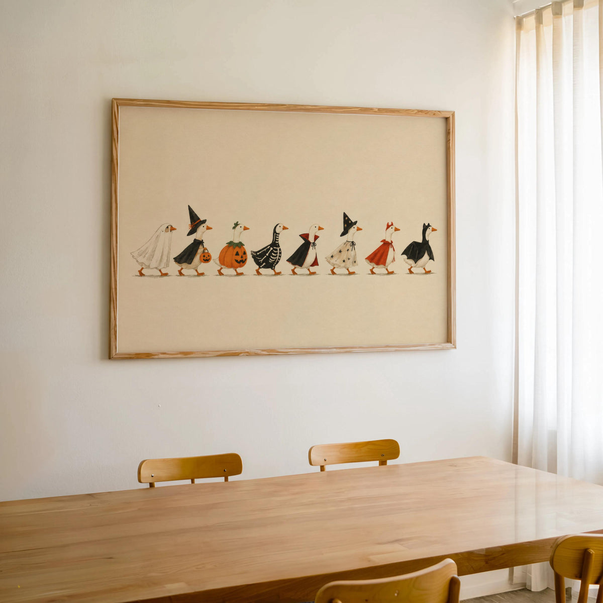 Framed Halloween duck print centered above dining table, warm cream paper, whimsical Halloween art for home