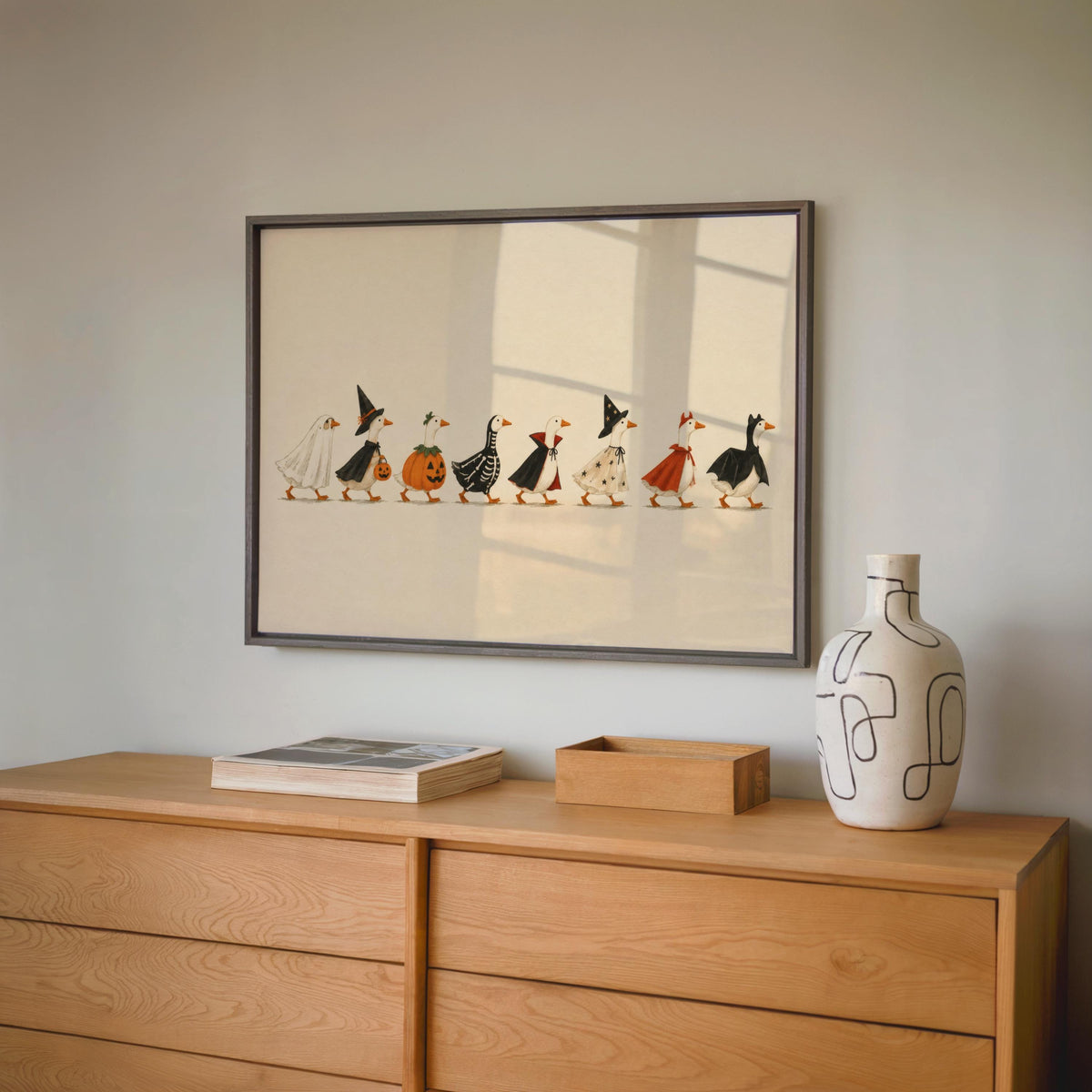 Framed Halloween parade print hung above oak credenza, muted earthy palette, storybook folk art ducks