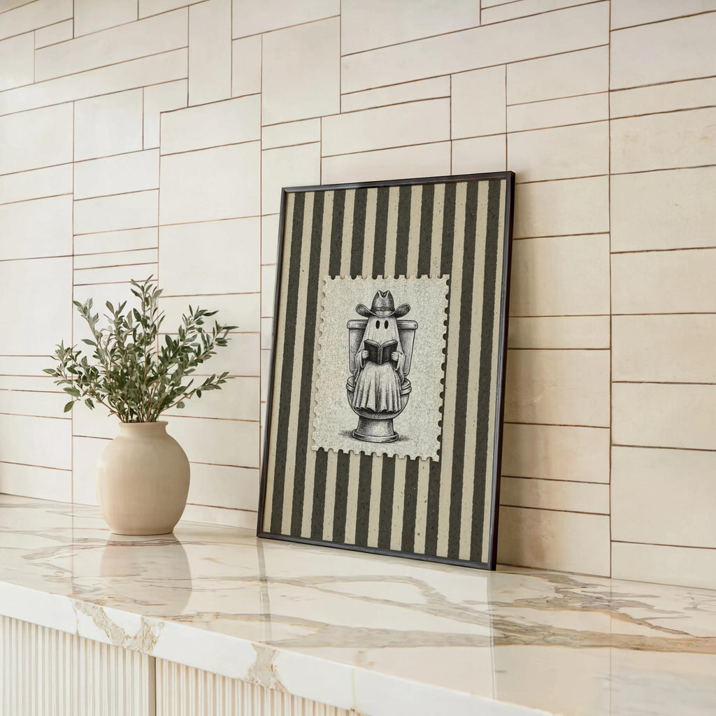 Striped ghost reading print leaning against shiplap wall beside a ceramic vase, antique Halloween illustration and spooky bathroom decor, funny bathroom wall art