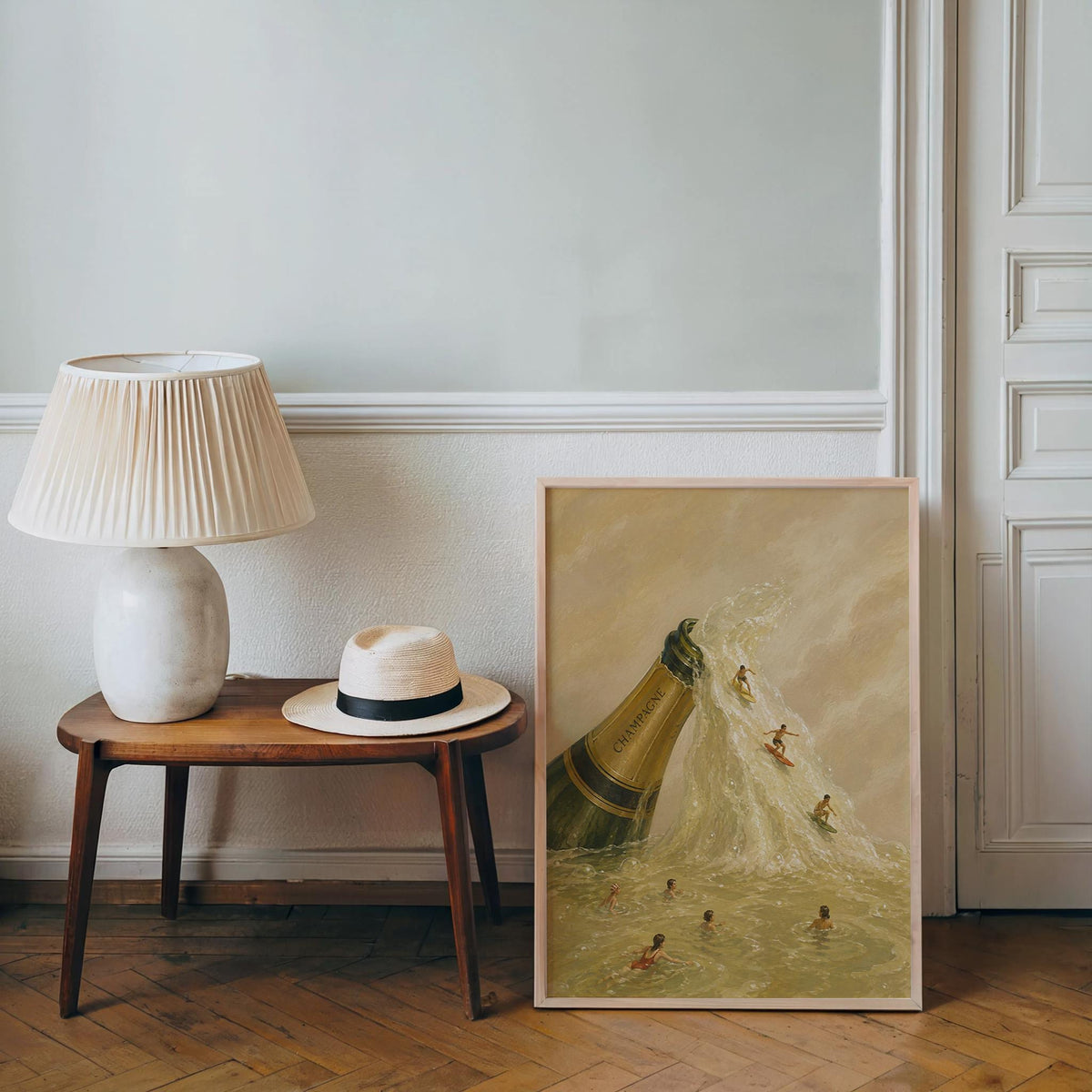 Champagne bottle wall art placed on floor by a lamp and hat, beige tones, whimsical miniature surfing scene