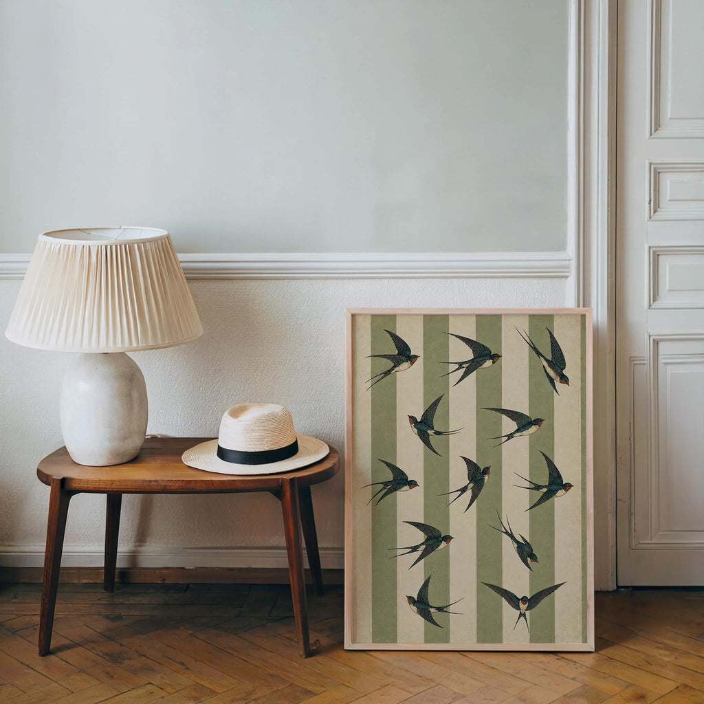 Framed swallow bird wall art resting beside a lamp and hat on a console, cozy cottagecore bird decor styling