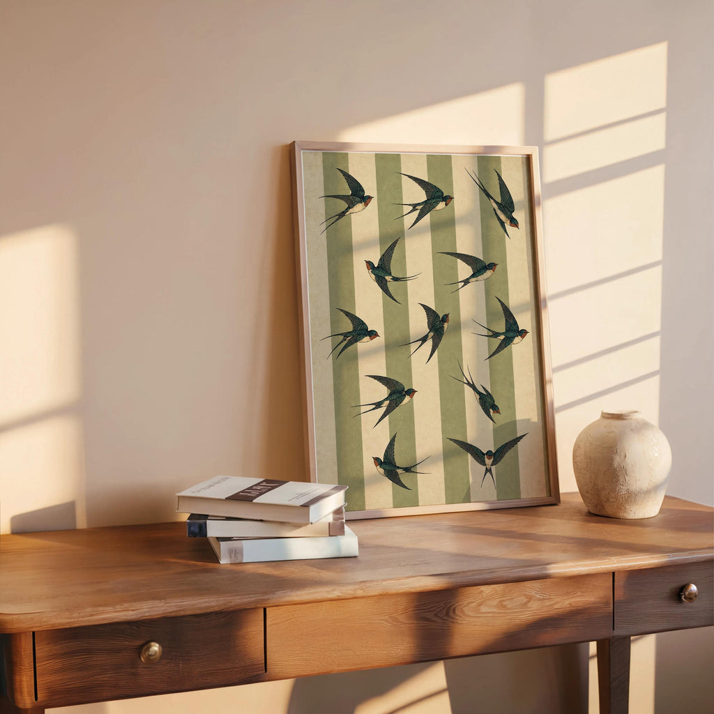 Warm desk vignette with framed swallow art print, green striped bird print paired with books for cottagecore decor