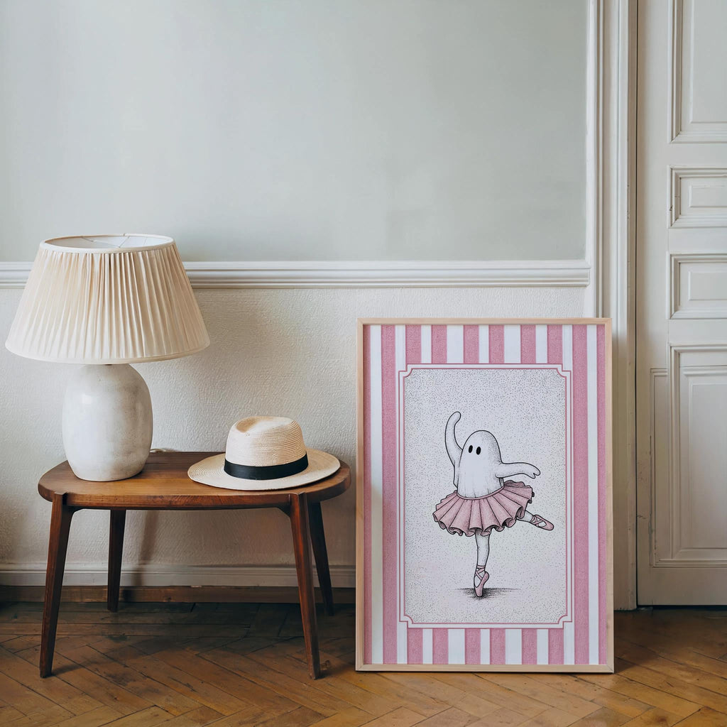 Ballerina ghost poster displayed beside a lamp and side table, pink nursery wall art for a cozy corner