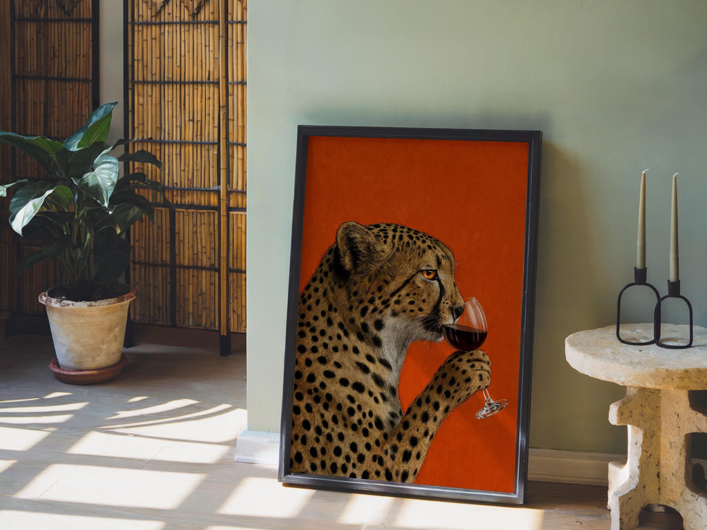 Cheetah drinking wine wall art propped on a sunlit floor, potted plant and candle holders, surreal vintage big cat print
