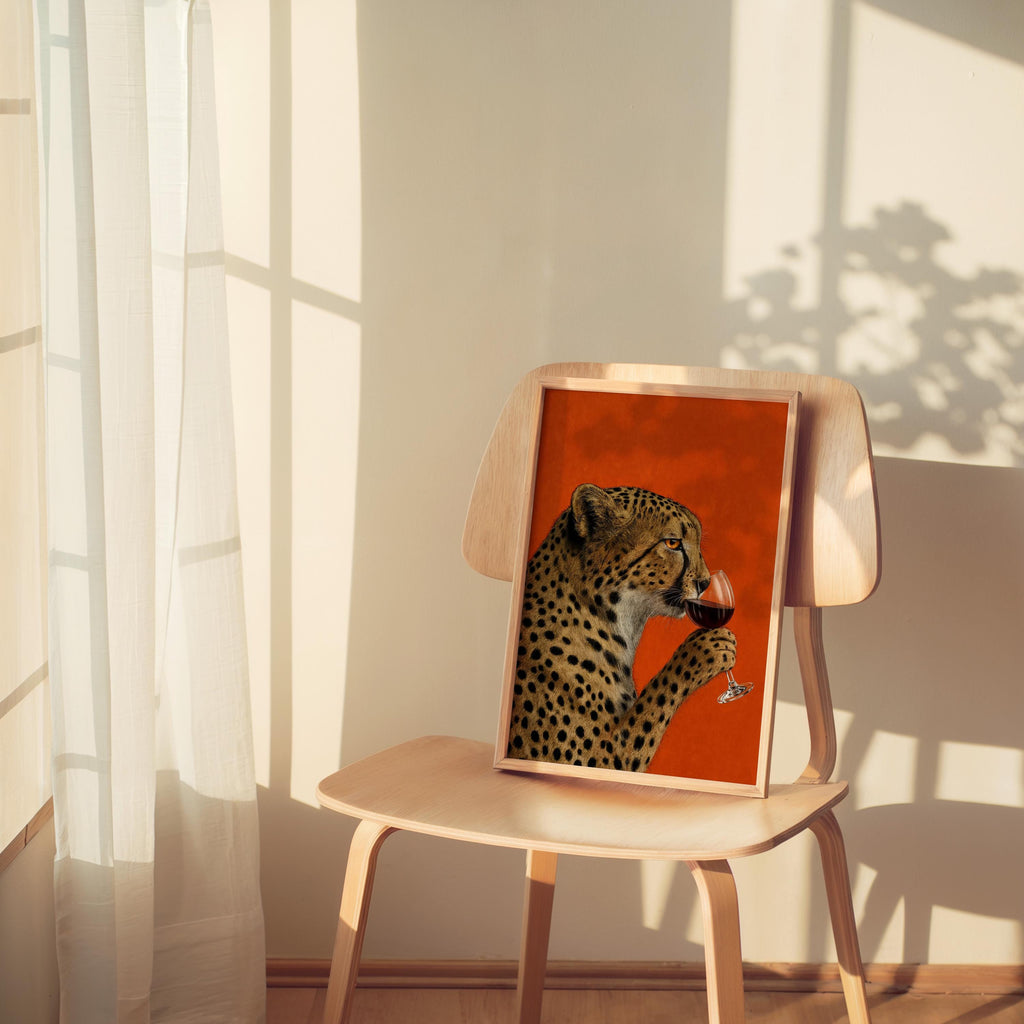 Smaller cheetah drinking wine wall art perched on a sunlit chair, funny cat wall art with retro, playful illustration