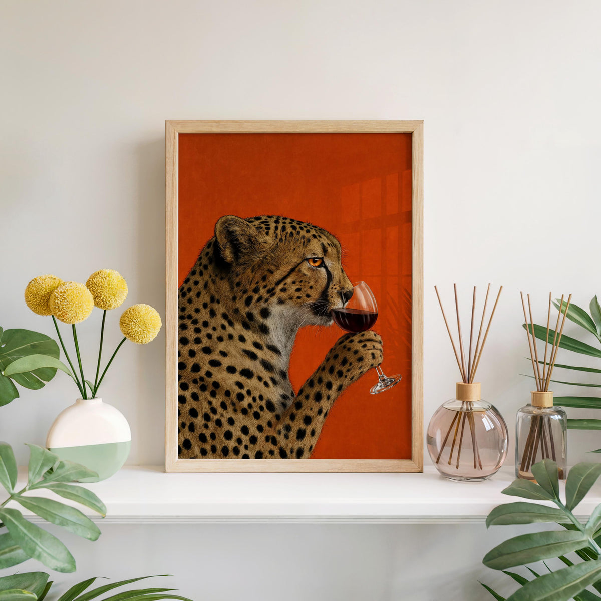Framed cheetah drinking wine wall art on a mantel with vases and greenery, vintage big cat print for red-focused rooms