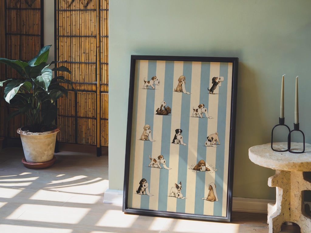 Frame resting on wood floor near plants, muted light on puppy toilet paper poster, funny dog bathroom wall art