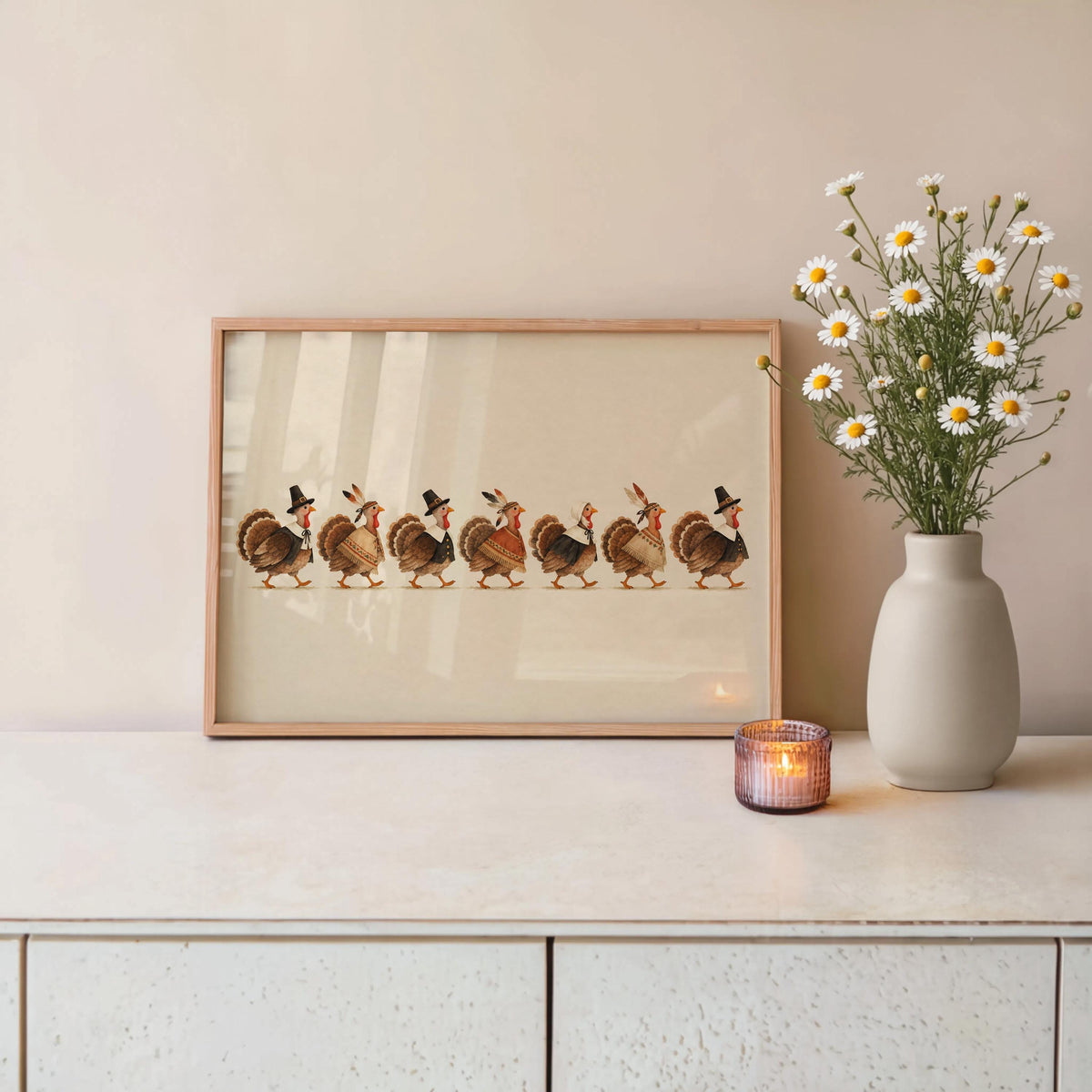 Low console styled with framed quirky turkey art print, vase of flowers and candle, warm cream backdrop