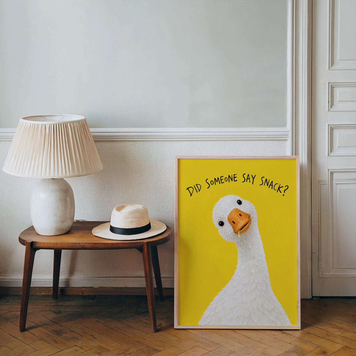 Framed print propped beside a midcentury lamp and small table, funny kitchen poster that doubles as pantry wall decor