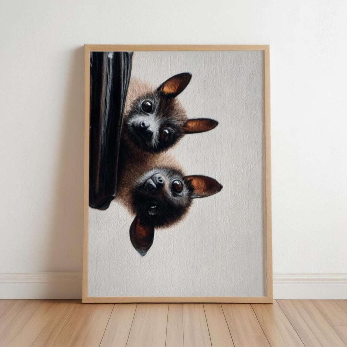 Framed fruit bat wall art leaning on pale wood floor, two fuzzy bats peeking from a branch