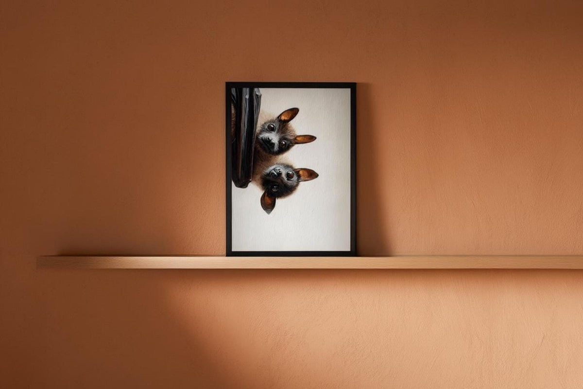 Small framed flying fox wall art resting on a thin shelf, warm amber light, cute bat print vibe
